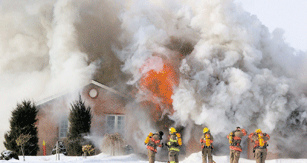Firefighters working in front of a home billowing smoke