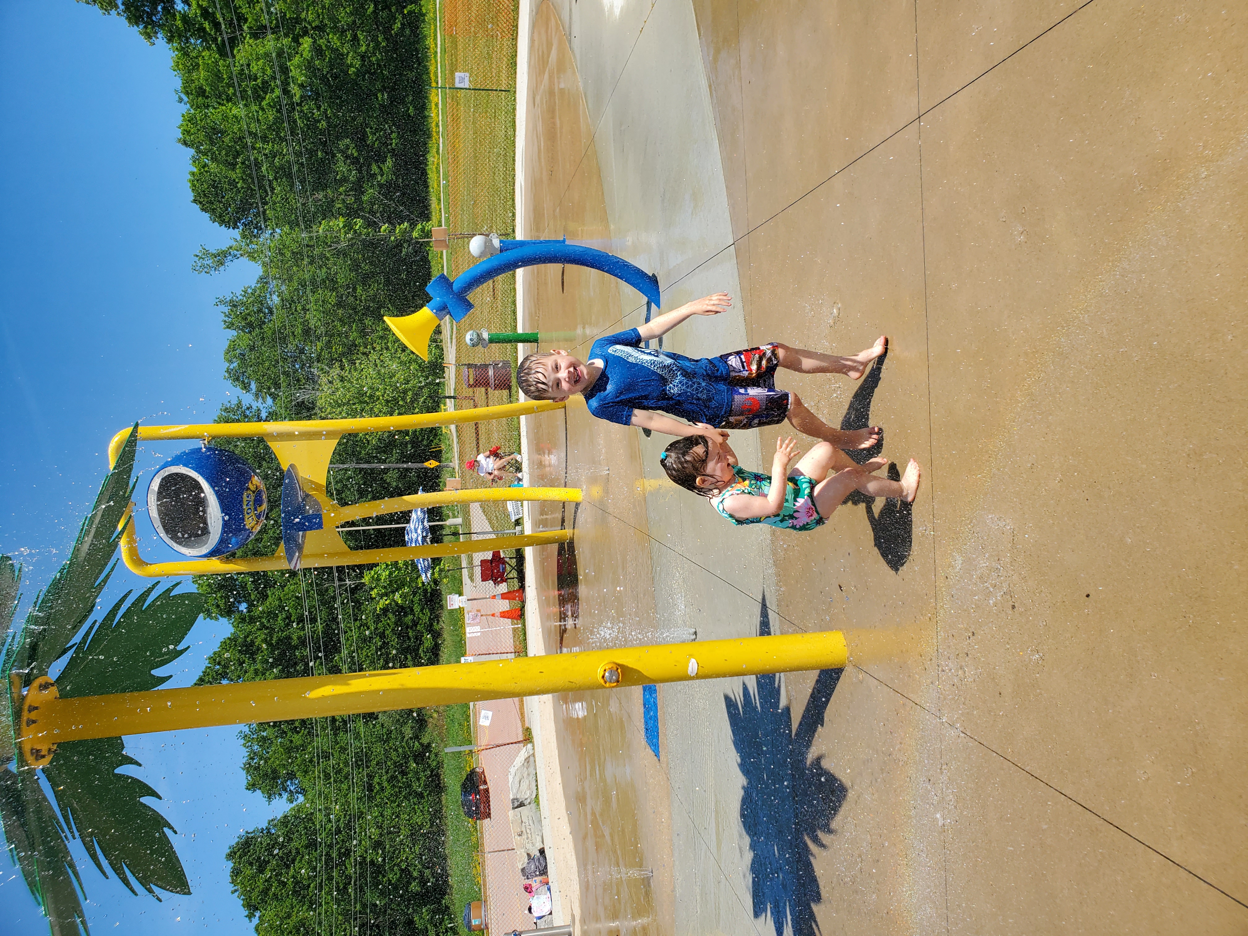 Two young children play in the splash pad under the tree water feature.